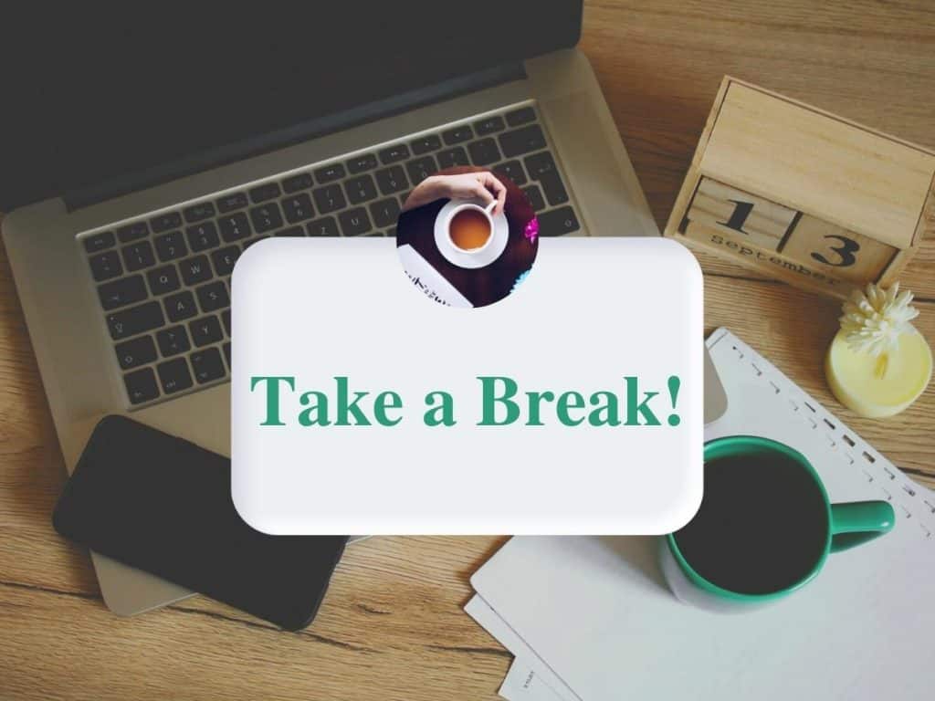 The words "Take a Break!" are overlayed a computer with a phone, green coffee mug, and wooden calendar blocks next to a candle.